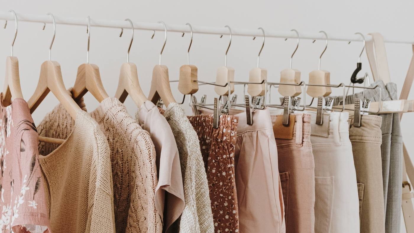 A rail of preloved knitwear, blouses and trousers in soft pinks and neutrals